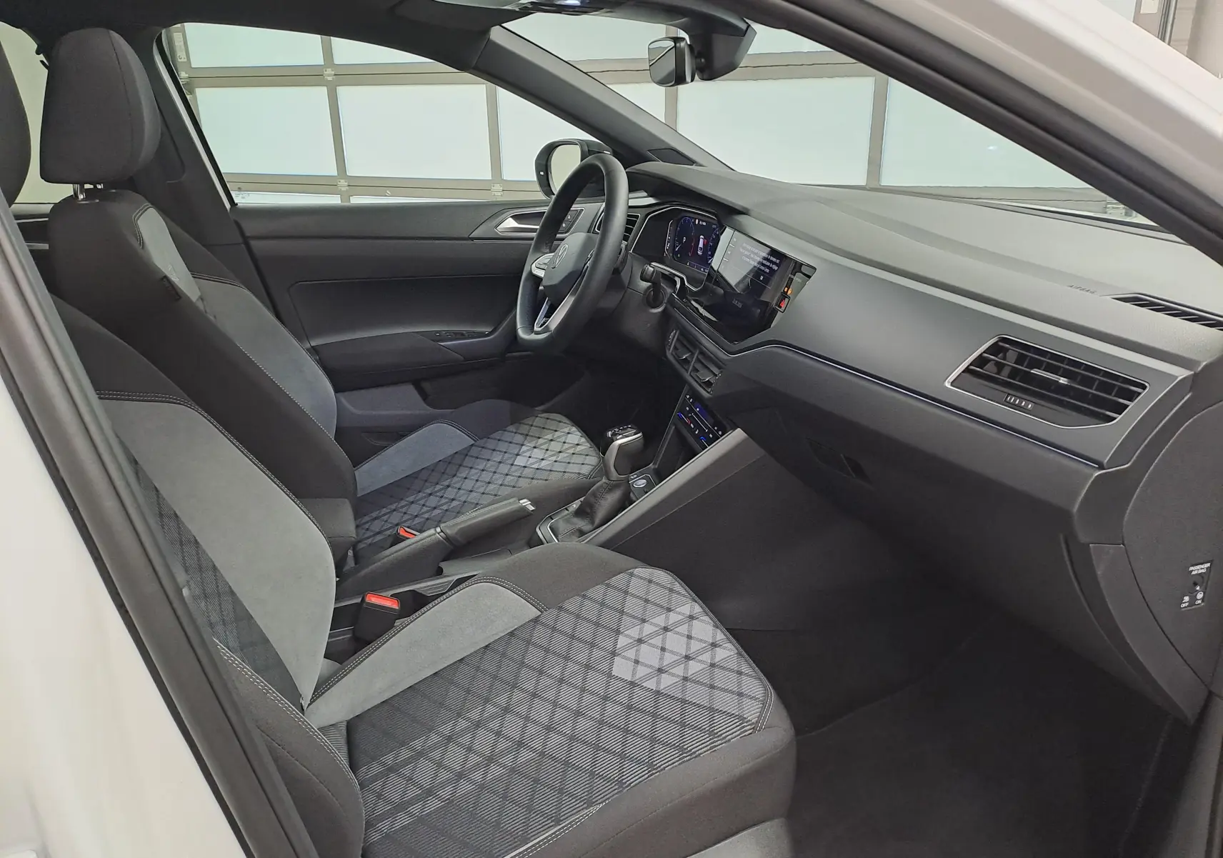 Vue intérieure côté conducteur du Volkswagen Taigo 1.5 TSI 2025, sièges tissu noir et gris avec motifs géométriques.