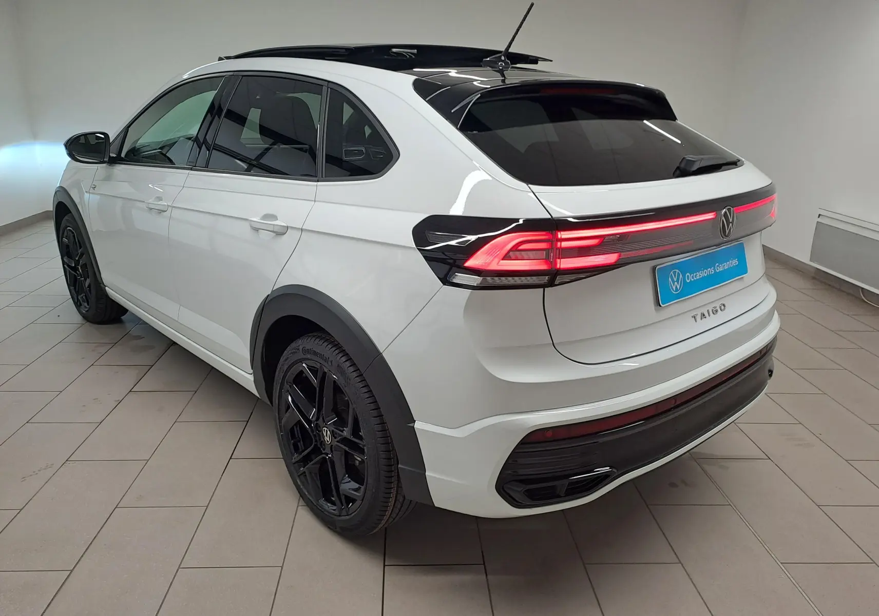 Vue 3/4 arrière droite du Volkswagen Taigo blanc pur avec toit noir et jantes noires R-Line dans un showroom.