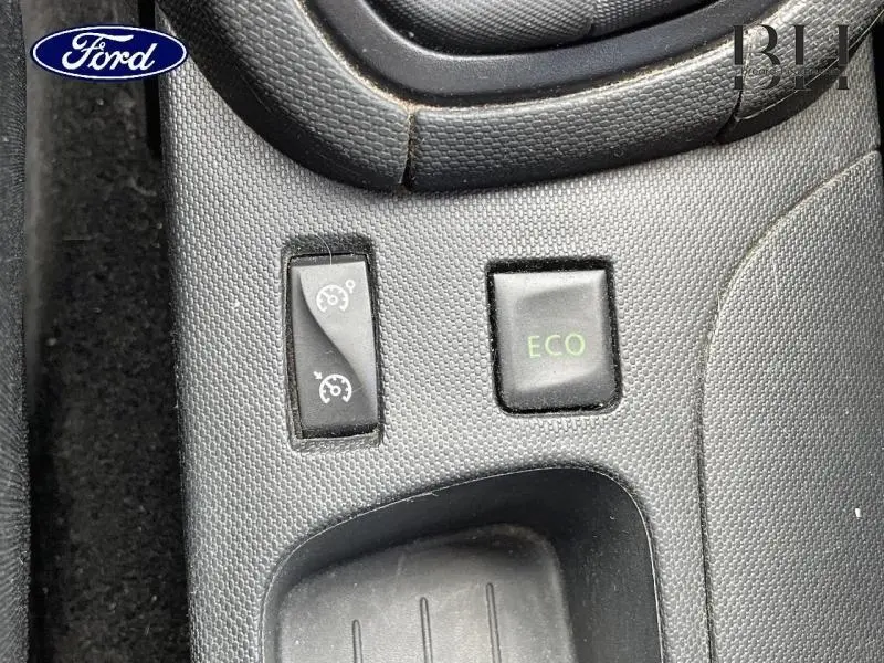 Gros plan sur les boutons de commande du régulateur de vitesse et mode ECO sur console centrale noire d’une Renault Clio gris Cassiopée.