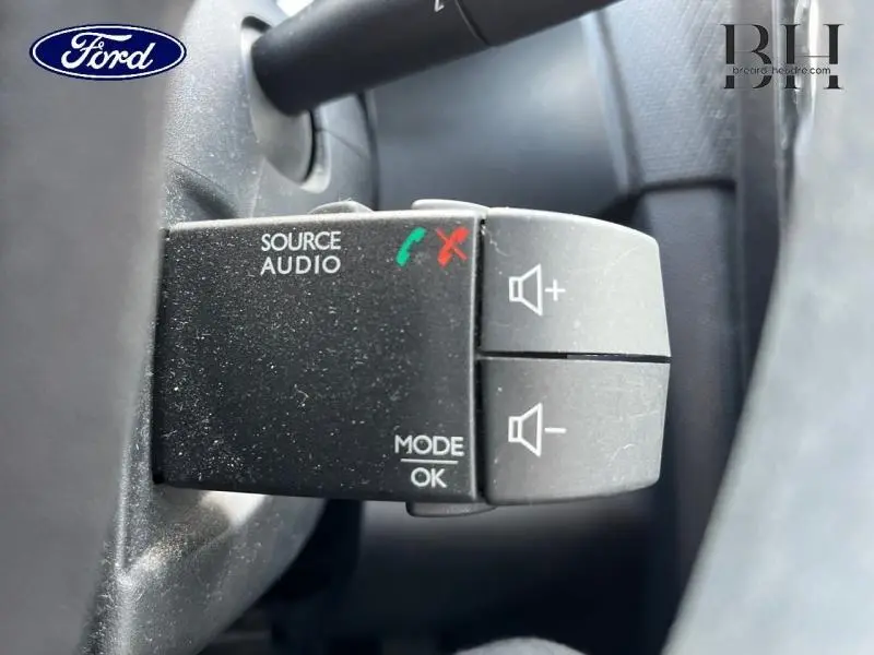 Gros plan sur la commande audio au volant d’une Renault Clio, boutons volume et mode, intérieur noir.