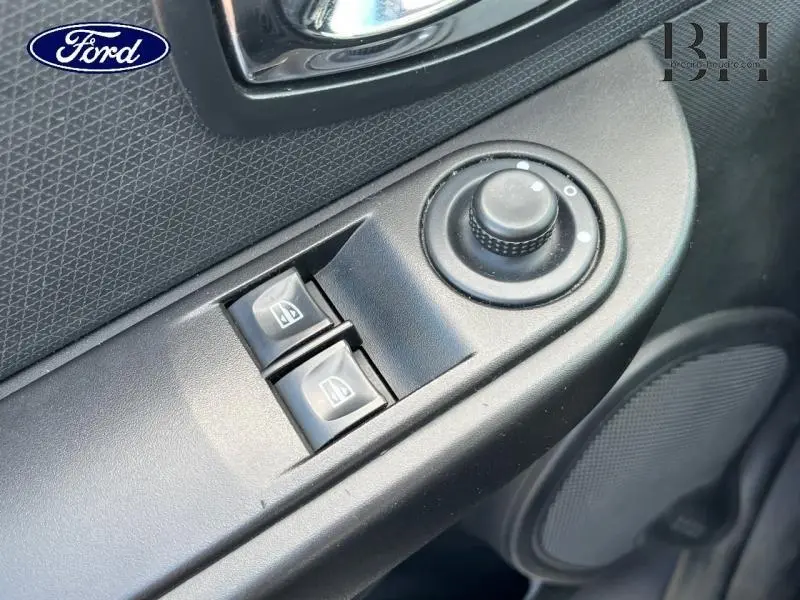 Détail des commandes de réglage des rétroviseurs et des vitres électriques côté conducteur, plastique noir texturé.