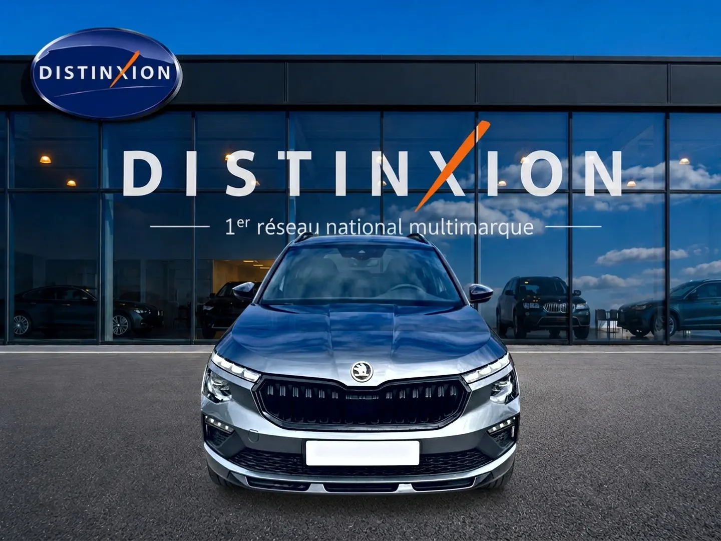 Vue frontale d'un Skoda Kamiq gris graphite 2026 avec calandre noire et phares LED devant un showroom Distinxion.