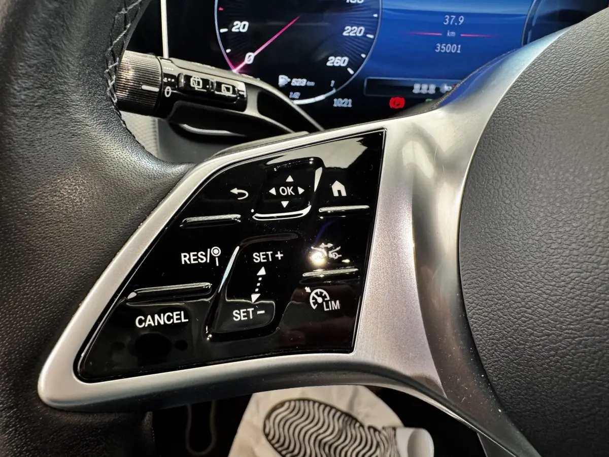 Gros plan sur les commandes du volant à gauche d’un Mercedes GLC 300 E Business Line gris foncé, tableau de bord numérique visible.