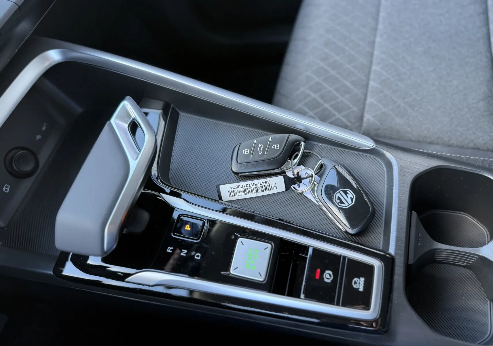 Gros plan sur la console centrale du MG ZS Hybrid 2026, avec levier de vitesse automatique et clés posées sur surface noire texturée.