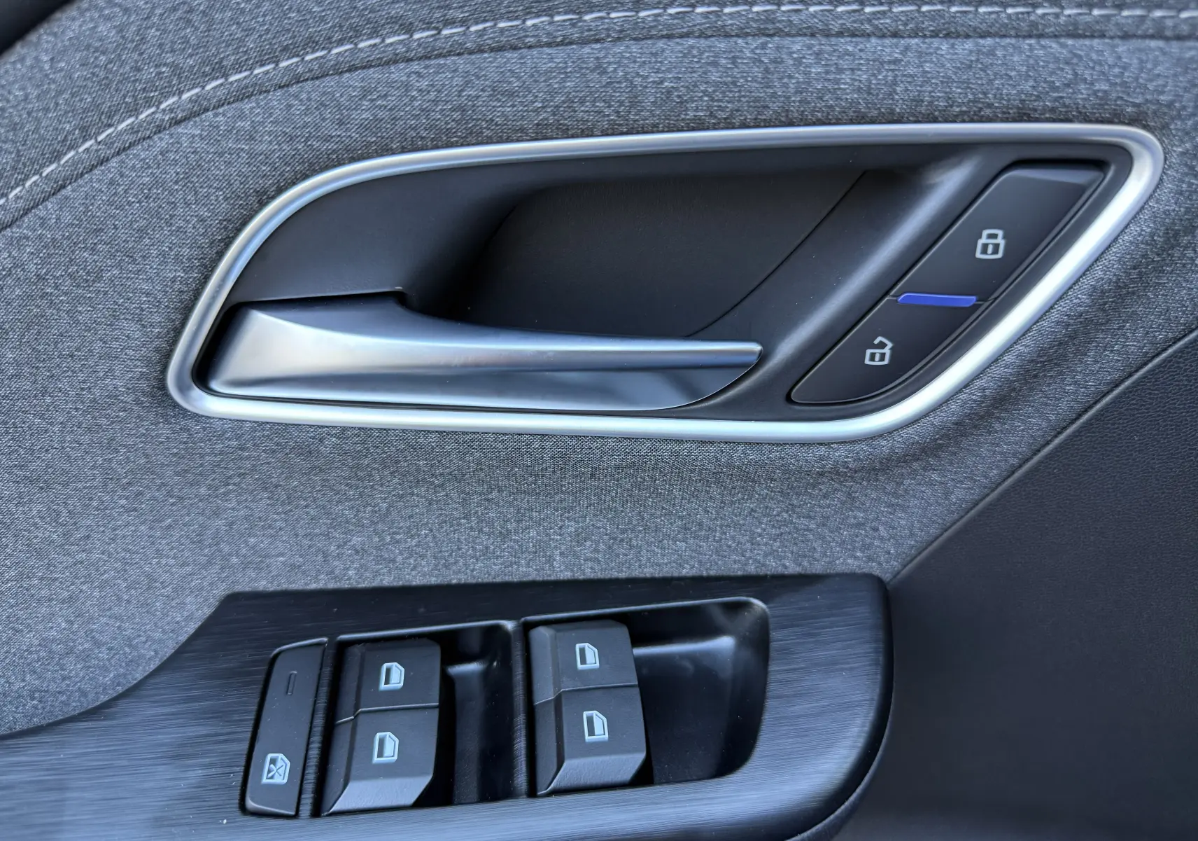 Gros plan sur la poignée intérieure et les commandes de fenêtre côté conducteur du MG Motor ZS Hybrid 197 gris foncé.