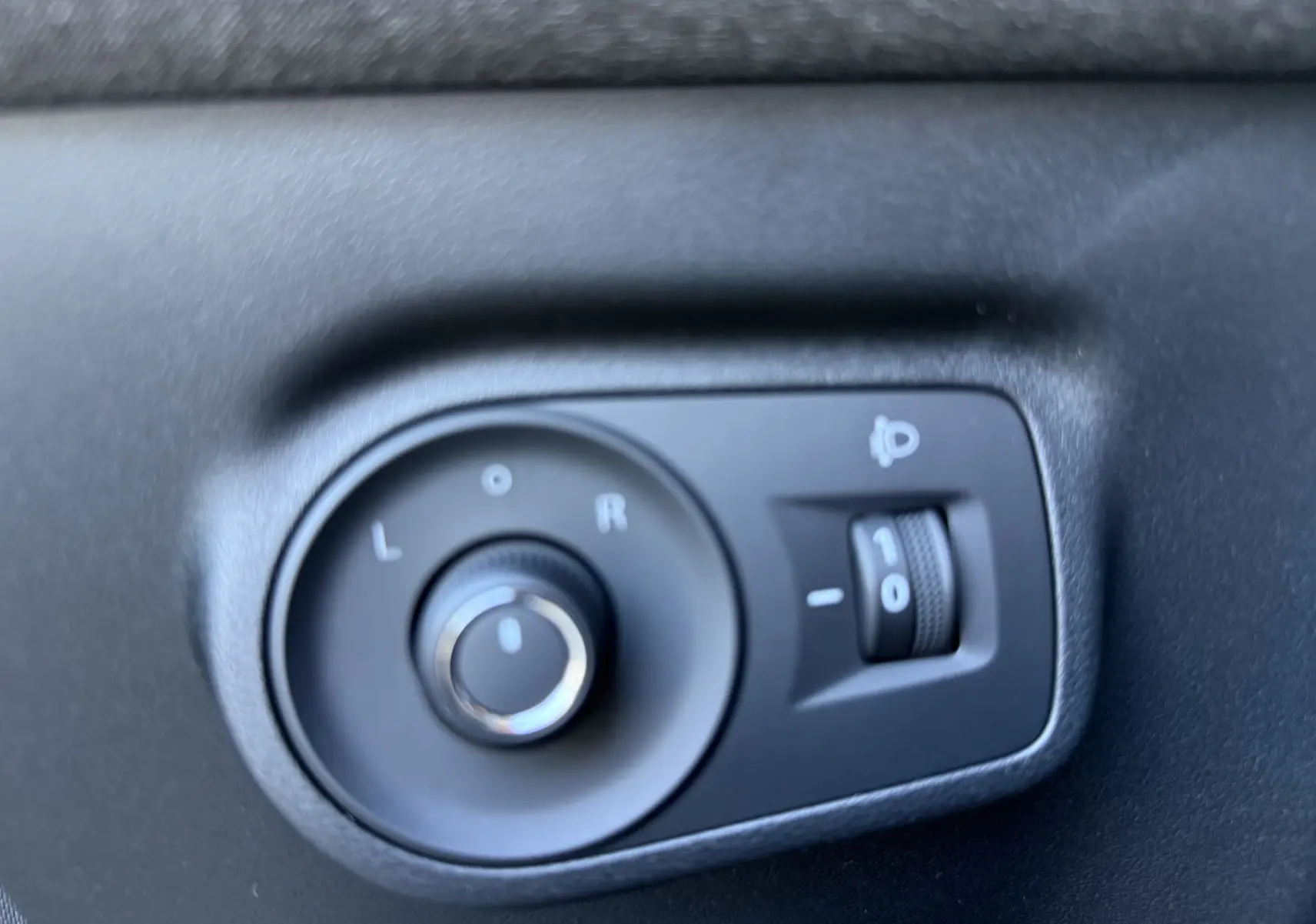 Gros plan sur les commandes de réglage des rétroviseurs électriques dans un MG Motor ZS Hybrid gris foncé, intérieur côté conducteur.