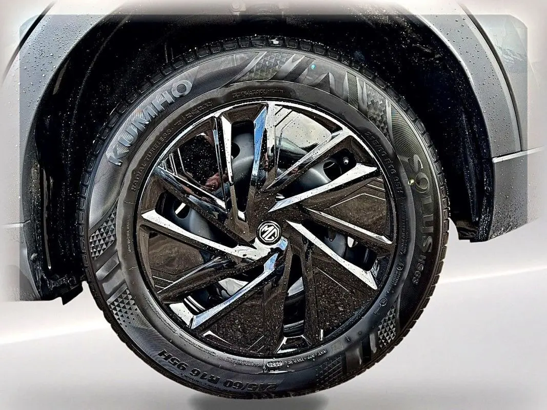 Gros plan sur la roue avant droite du MG ZS Hybrid 197 gris foncé avec jante noire brillante et pneus Kumho mouillés.