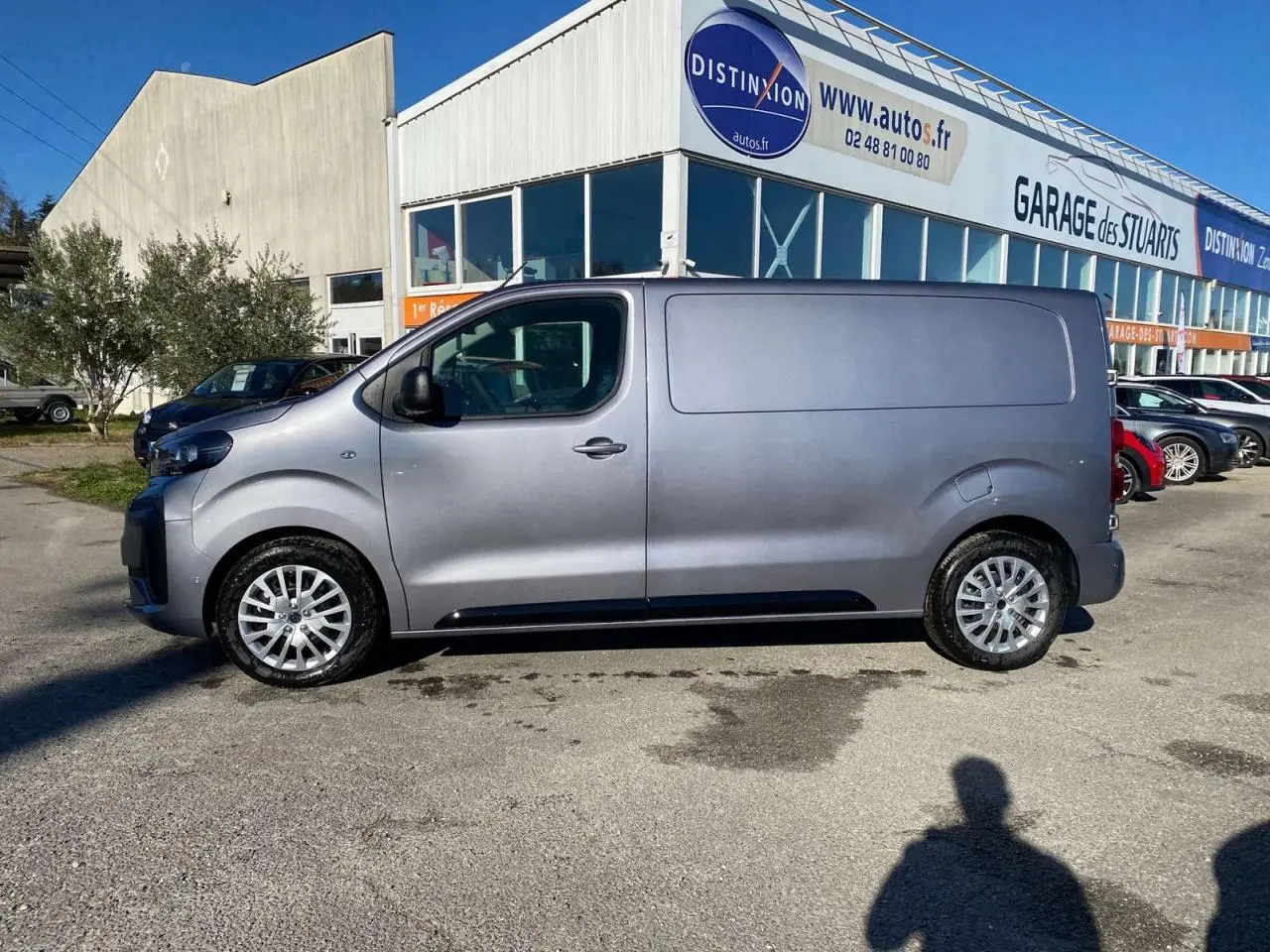 Peugeot Expert Fourgon gris Artense vu de profil côté gauche, stationné devant un garage en extérieur.
