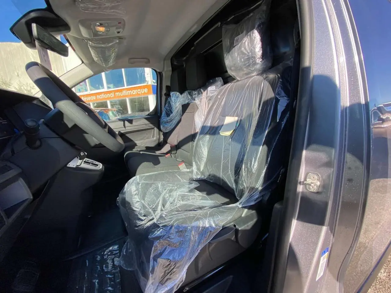 Vue intérieure côté conducteur du Peugeot Expert Fourgon gris Artense, sièges avant protégés par film plastique.