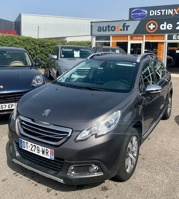 Peugeot 2008 gris foncé vue 3/4 avant droit, avec calandre chromée et toit noir, stationnée devant un concessionnaire autos.fr