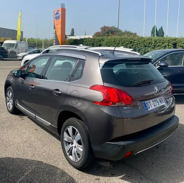 Peugeot 2008 gris métallisé vue en 3/4 arrière droit, avec barres de toit et feux arrière distinctifs.