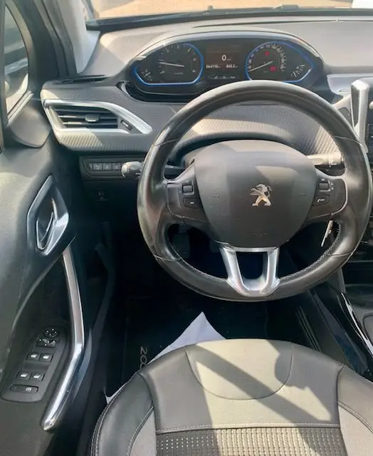 Vue intérieure frontale du tableau de bord et volant Peugeot 2008 gris, avec compteurs numériques et commandes au volant visibles.