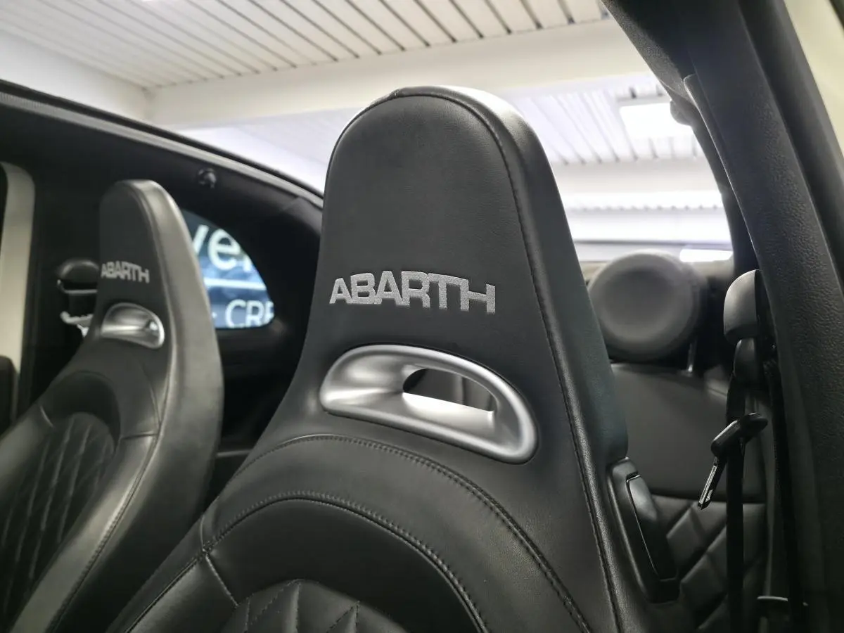 Gros plan sur les sièges avant en cuir noir avec logo ABARTH brodé, intérieur de l'Abarth 595C Turismo blanc.