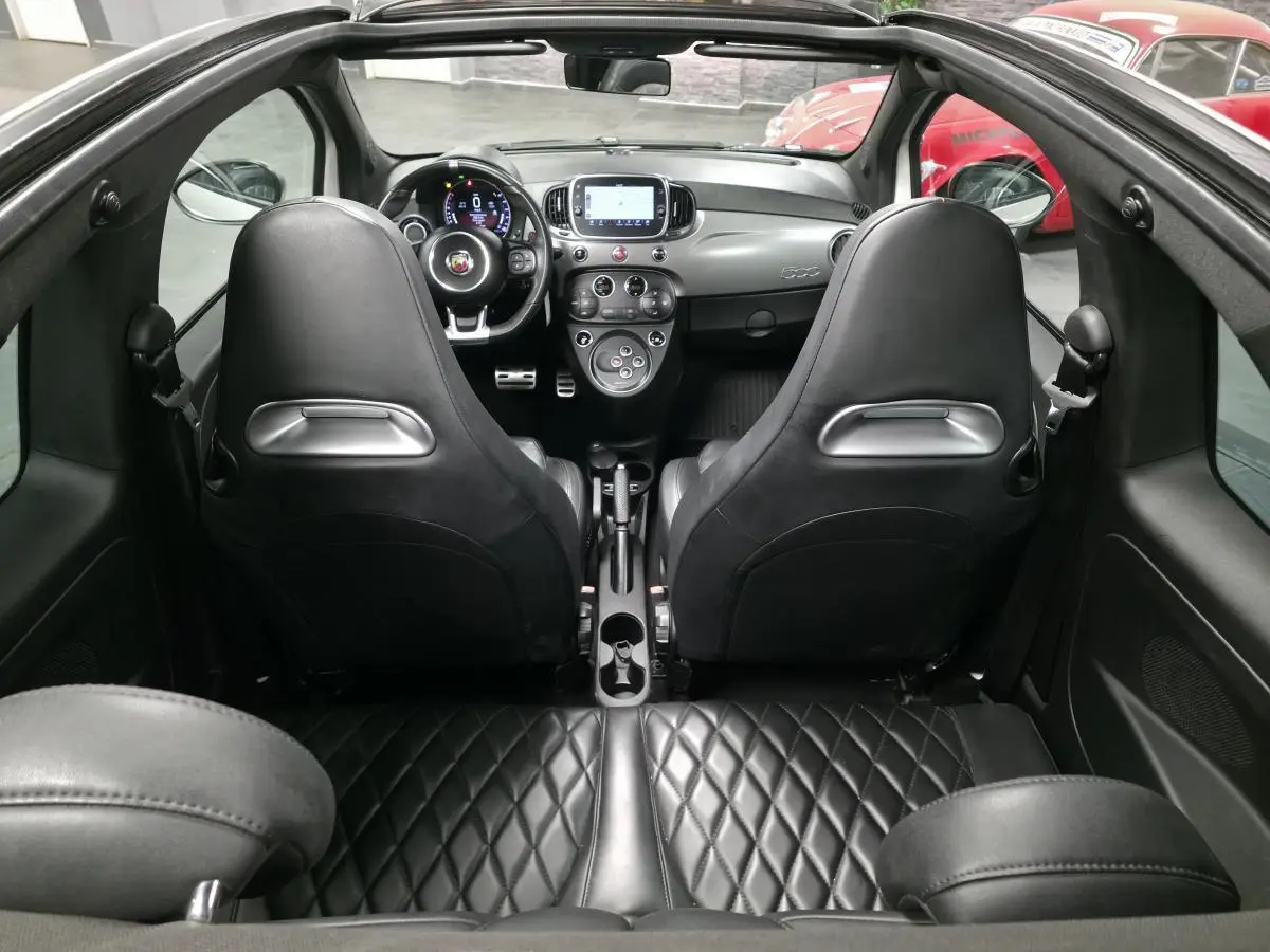 Vue intérieure arrière de l'Abarth 595C Turismo 2021, sellerie cuir noire matelassée et tableau de bord gris satiné.