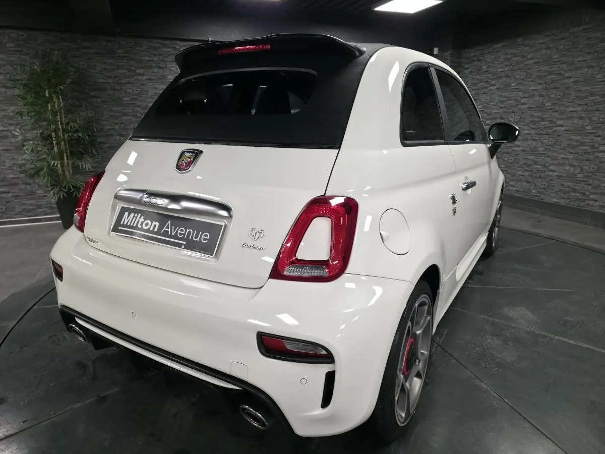 Vue 3/4 arrière droite de l'Abarth 595C Turismo blanche avec toit noir et étriers de frein rouges visibles.