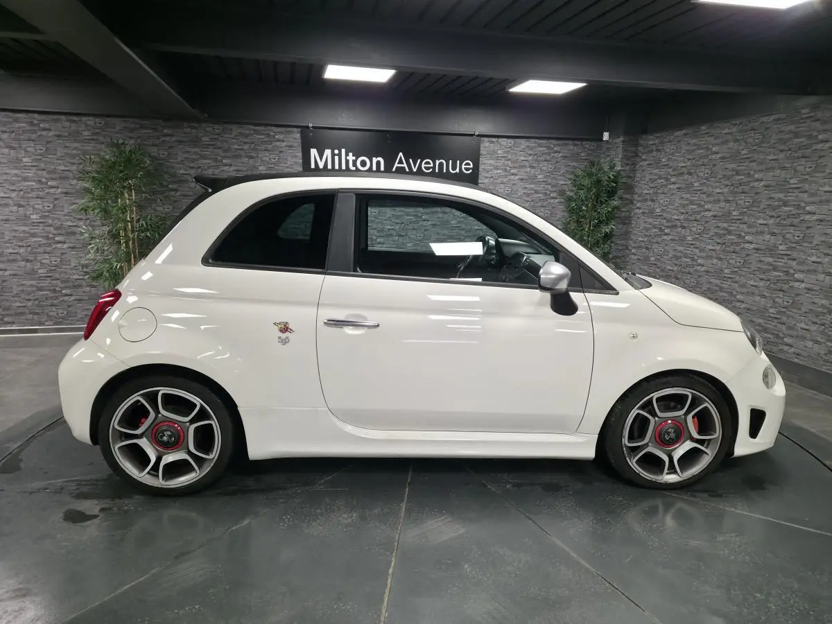 Profil droit d'une ABARTH 500 blanche avec jantes 17 pouces et étriers de frein rouges, dans un showroom intérieur.