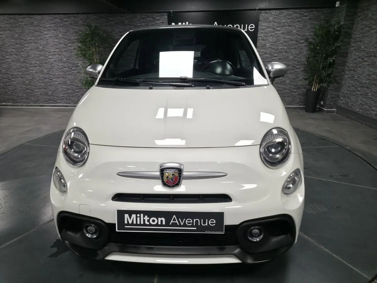 Vue frontale d'une Abarth 500 blanche avec calandre nid d'abeille et logo Abarth visible au centre.