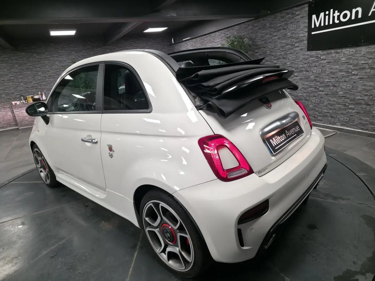 Vue 3/4 arrière droite d'une ABARTH 595C Turismo blanche avec toit ouvrant replié et étriers de frein rouges.
