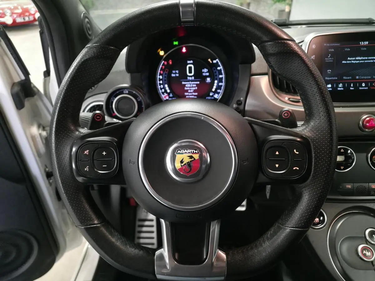 Vue centrée sur le volant cuir perforé noir de l'Abarth 595C blanc, avec tableau de bord numérique et écran tactile visible.