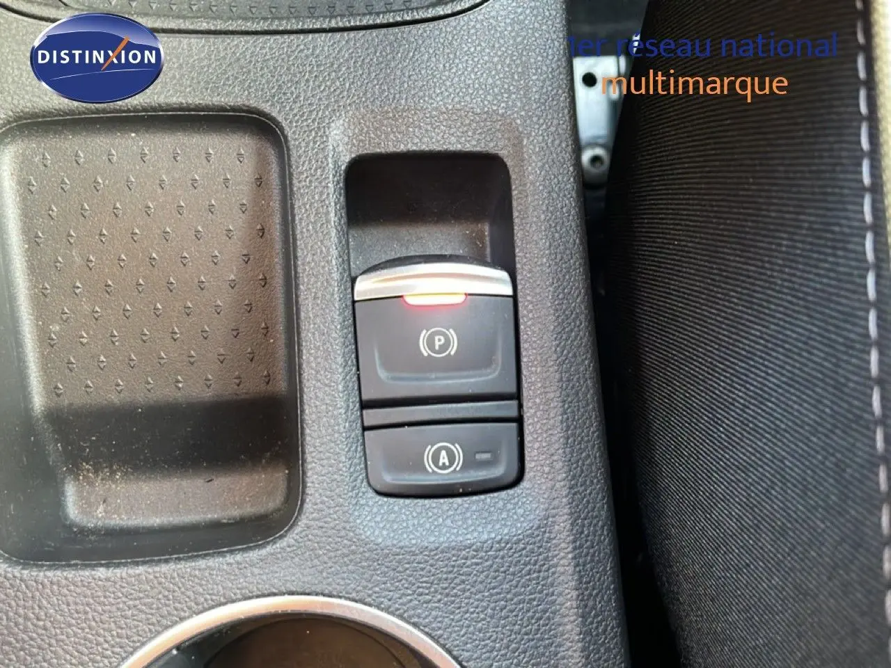 Gros plan sur la console centrale avec les commandes de frein à main électronique et arrêt auto, intérieur tissu noir.