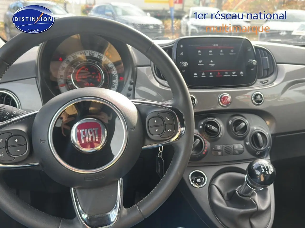 Vue intérieure centrée sur le volant noir et la console centrale grise avec écran tactile et levier de vitesses manuel.