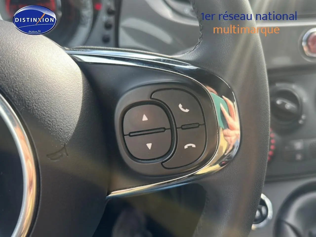 Gros plan sur les commandes audio au volant cuir de la FIAT 500 gris, avec tableau de bord flou en arrière-plan.