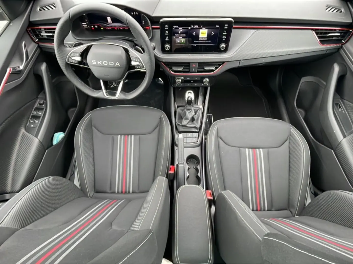 Vue intérieure frontale du Skoda Kamiq Monte Carlo 2026, sièges sport noirs avec bandes rouges et tableau de bord moderne.