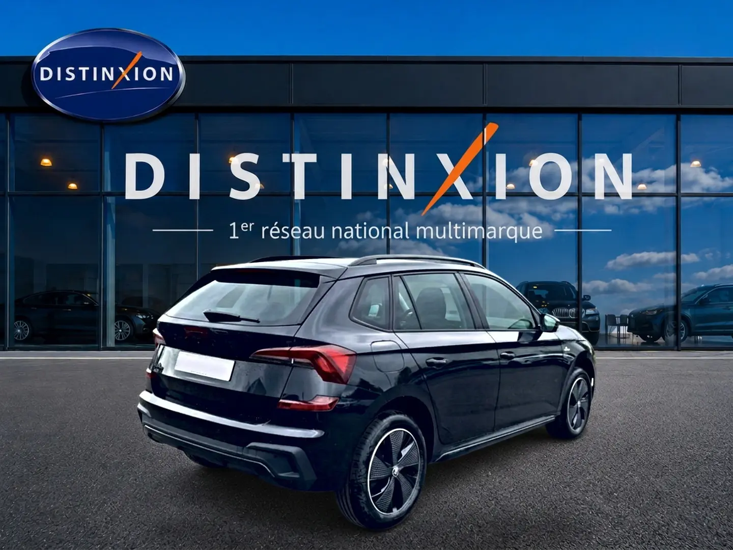 Vue 3/4 arrière droite d'un Skoda Kamiq noir 2026 avec jantes alu et barres de toit devant une vitrine Distinxion.