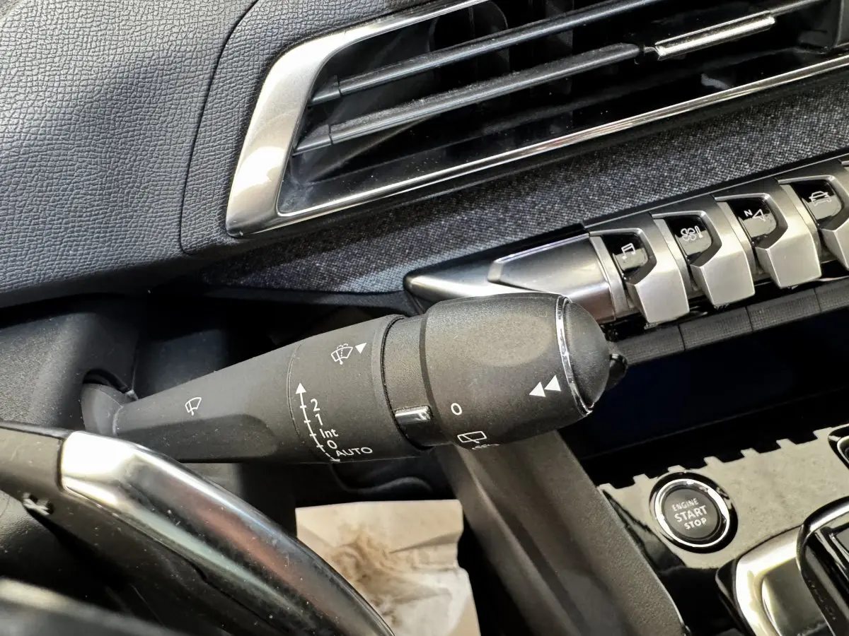 Gros plan sur la commande d’essuie-glace noire et les boutons de la console centrale d’un Peugeot 5008 noir, intérieur avant.