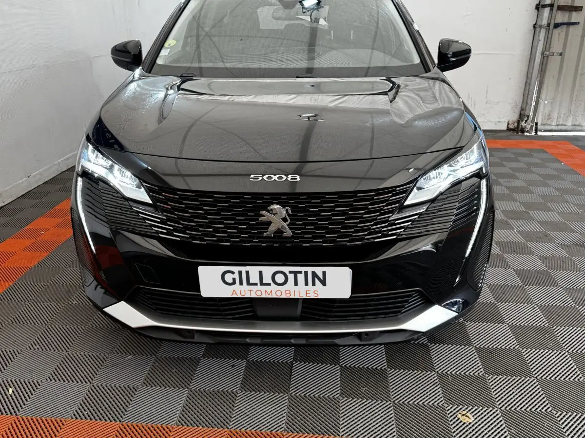 Vue frontale d'un Peugeot 5008 noir 2022 avec calandre distinctive et phares LED allumés dans un garage.