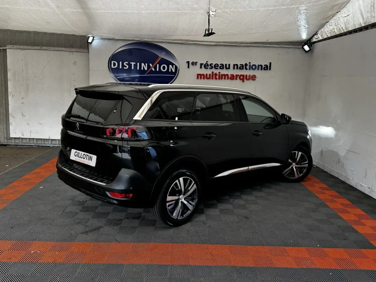 Peugeot 5008 noir vue 3/4 arrière droit dans un garage avec bandeaux chromés et jantes alliage visibles.