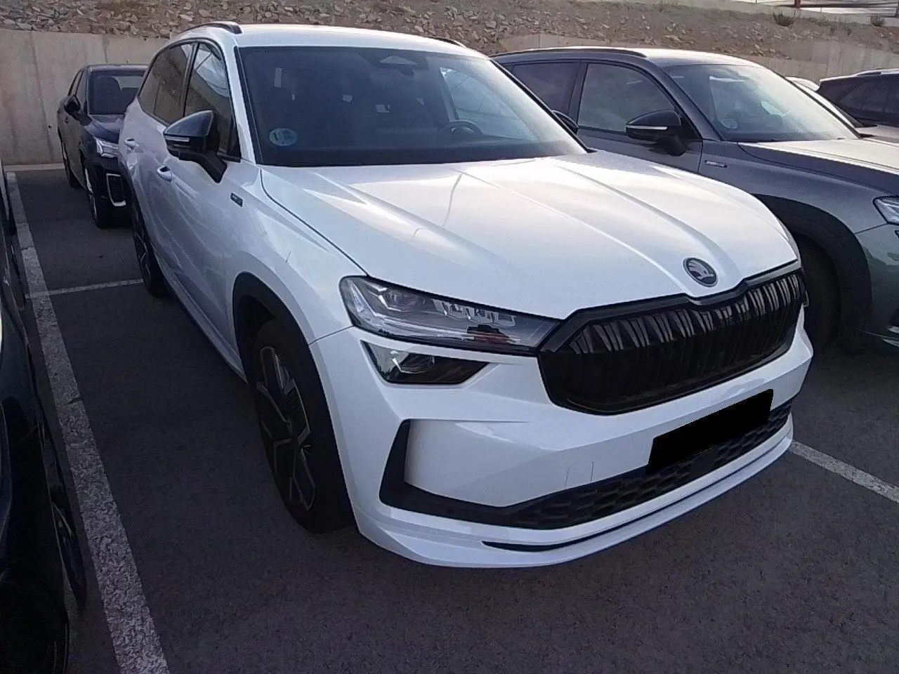 Vue 3/4 avant d'un Skoda Kodiaq blanc Glacier avec calandre noire et jantes alliage anthracite, stationné en extérieur.