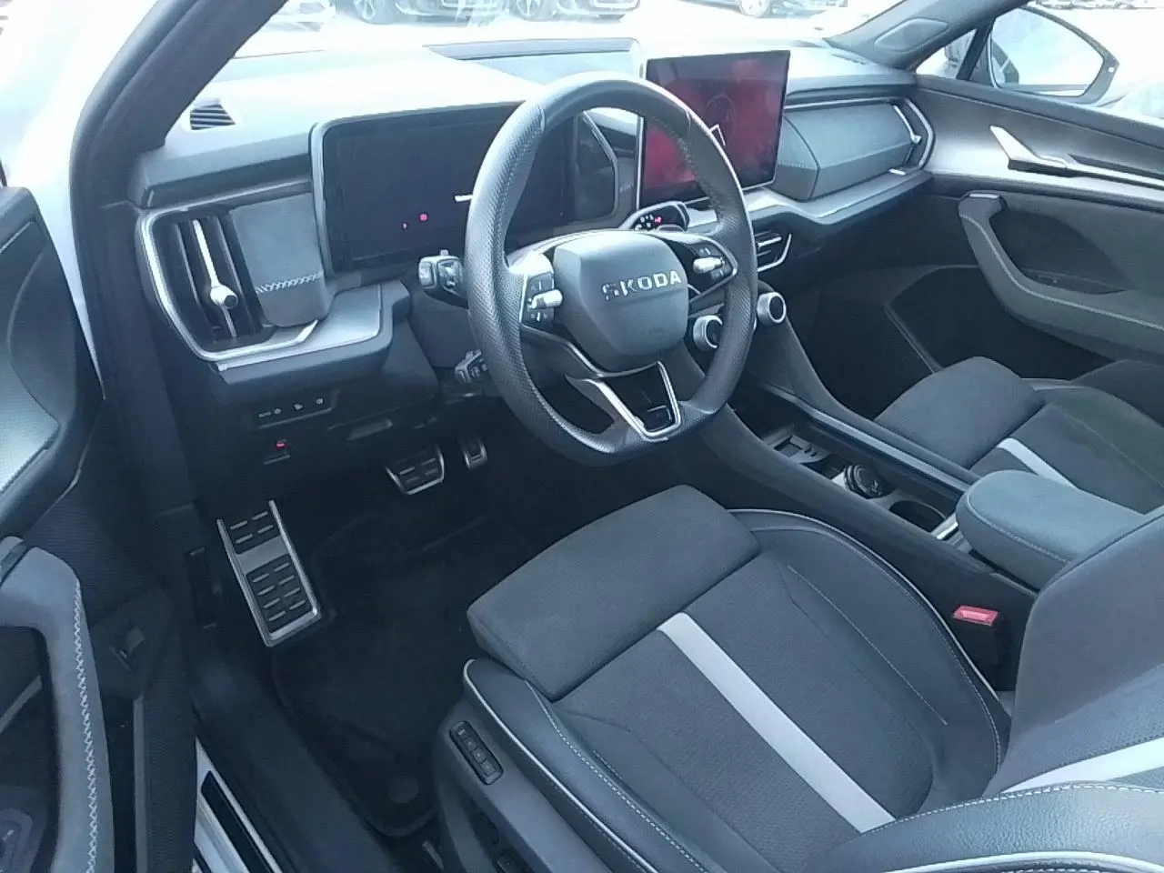 Vue intérieure côté conducteur du Skoda Kodiaq 2025, volant sport, sièges tissu suédine noir avec bande blanche, tableau de bord moderne.