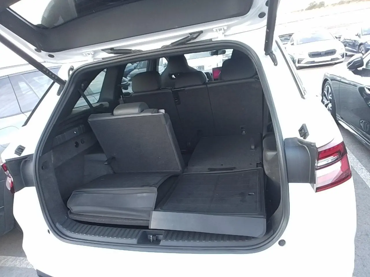 Vue arrière du Skoda Kodiaq blanc Glacier 2025 avec hayon ouvert et banquette arrière partiellement rabattue.