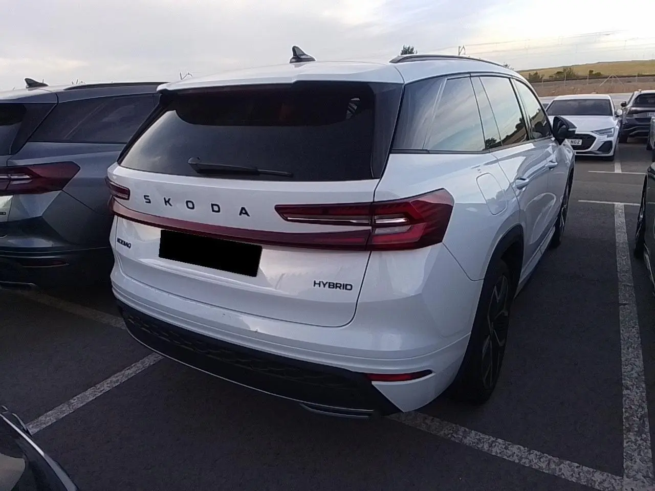 Vue 3/4 arrière droite d’un Skoda Kodiaq blanc Glacier hybride avec feux arrière LED et vitres surteintées.