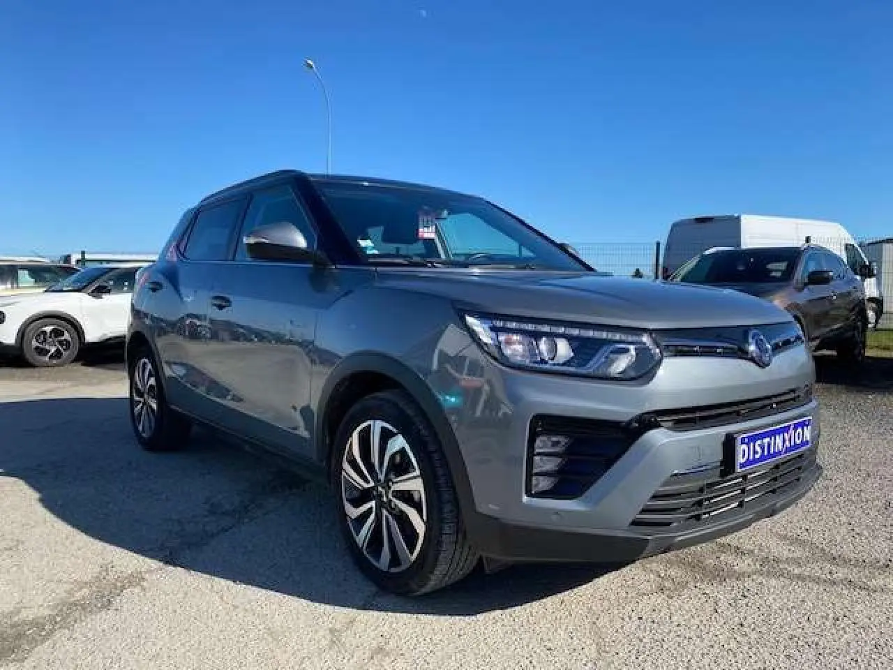 Ssangyong Tivoli gris foncé en vue 3/4 avant droit, avec jantes alliage et calandre moderne sous un ciel bleu.