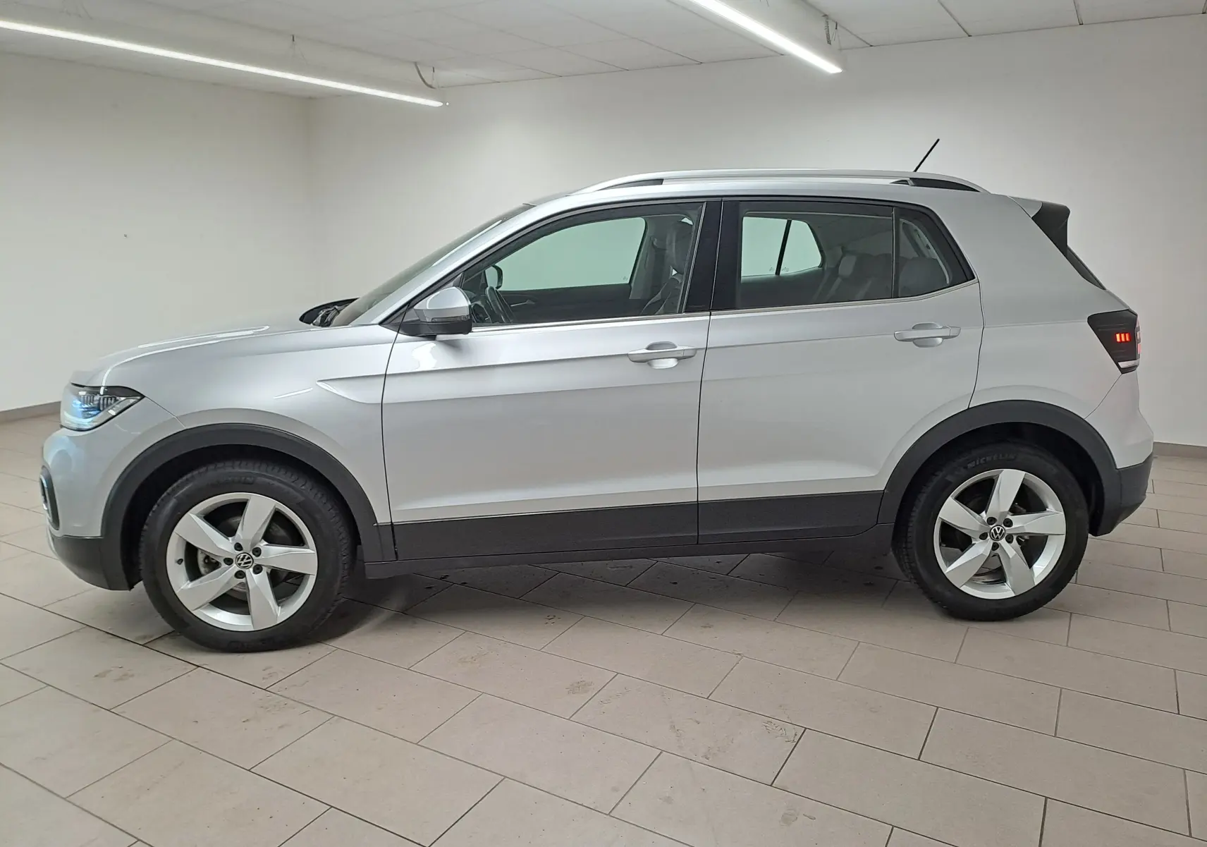Vue de profil côté gauche d'un Volkswagen T-Cross 2022 en peinture métallisée reflet d'argent dans un intérieur neutre.