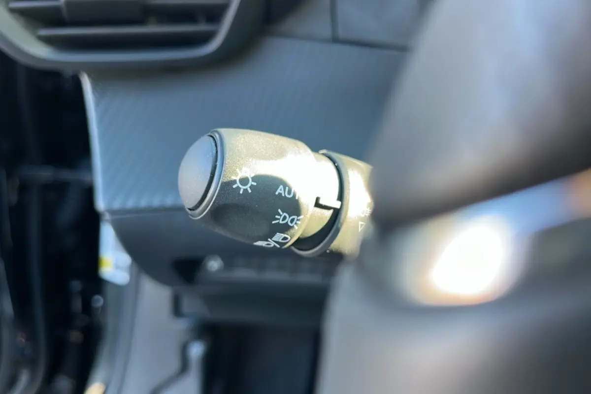 Gros plan sur la commande des feux au volant d’un Peugeot 2008 noir perla nera, intérieur moderne et lumineux.