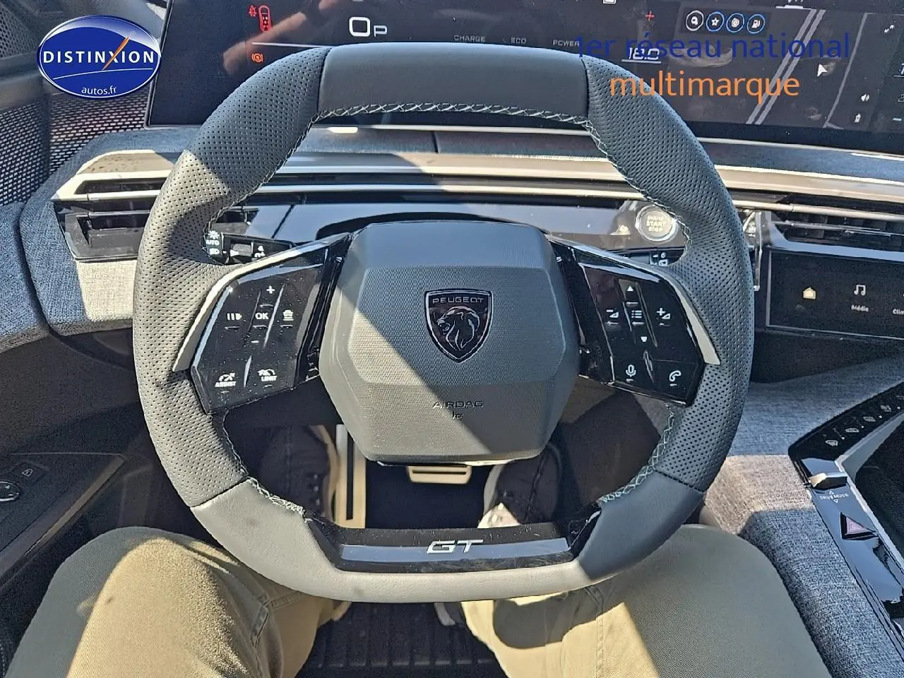 Vue intérieure centrée sur le volant cuir perforé gris du Peugeot 5008 Hybrid 145 GT avec tableau de bord numérique.