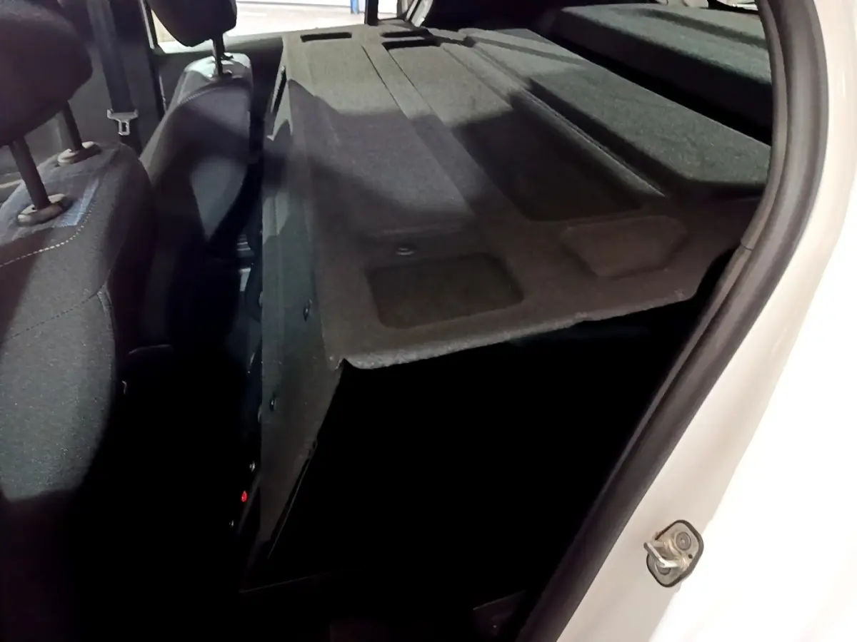 Vue intérieure arrière droite du coffre ouvert d'une Peugeot 208 blanche, montrant la banquette arrière rabattue et l'espace de chargement.