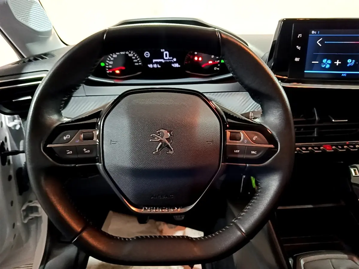 Vue rapprochée du volant noir de la Peugeot 208 1.5 BlueHDi 100 S&S Premium avec tableau de bord et écran tactile visibles.