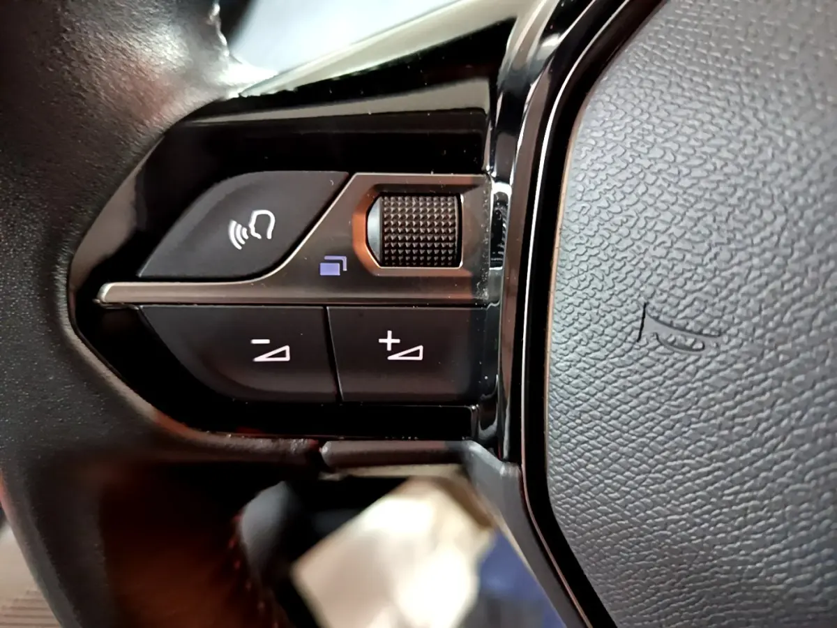 Gros plan sur les commandes vocales et volume au volant noir de la Peugeot 208 1.5 BlueHDi 2021.