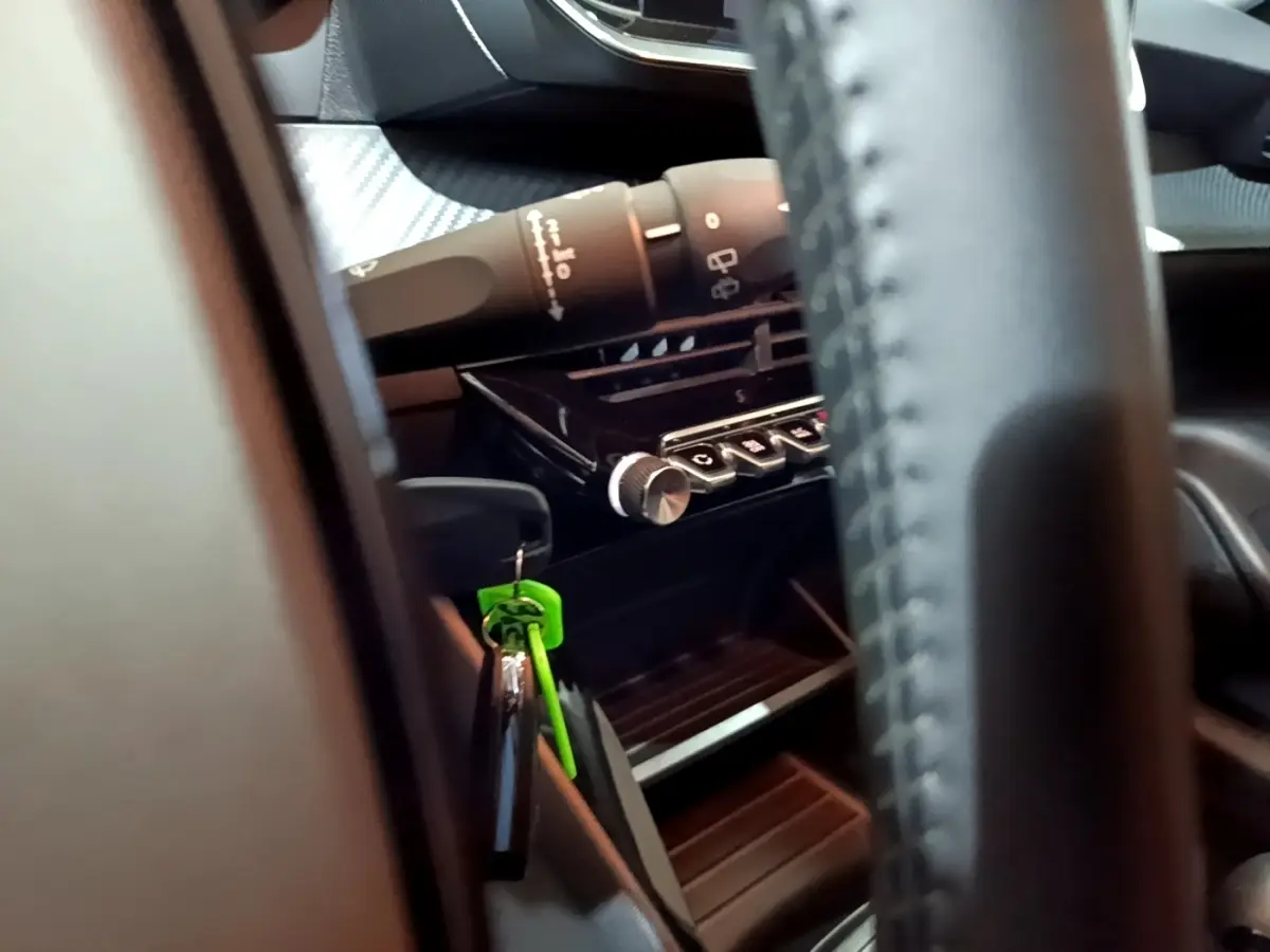Détail intérieur du tableau de bord et commandes de la Peugeot 208 blanc, avec clé verte suspendue près du volant.