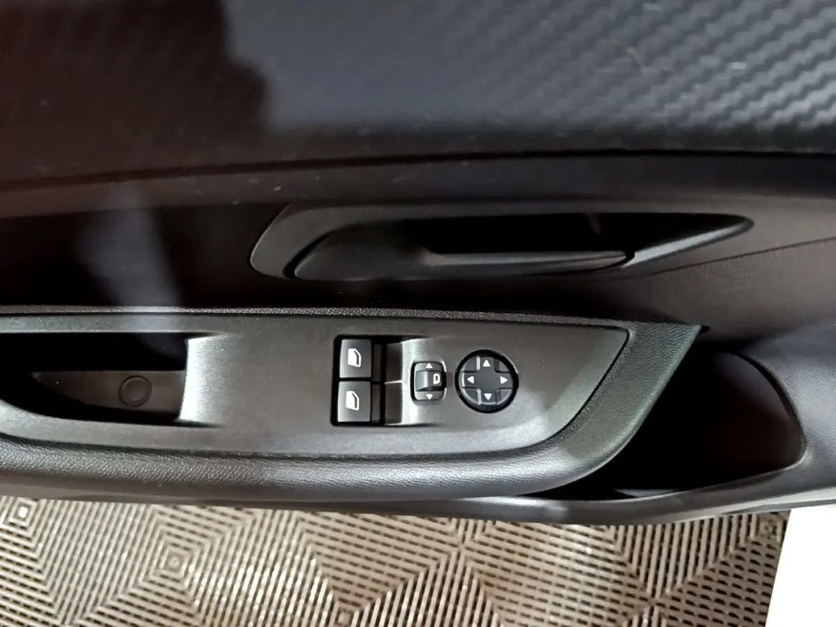 Gros plan sur les commandes de réglage des rétroviseurs et des vitres côté conducteur d'une Peugeot 208 blanche.