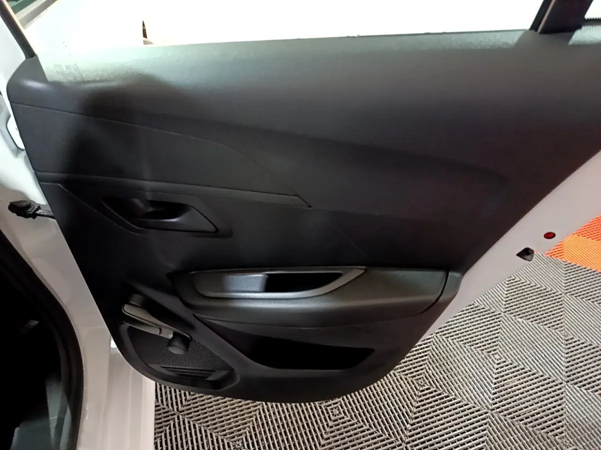 Vue rapprochée de la porte arrière gauche noire intérieure d’une Peugeot 208 blanche, avec poignée et commande manuelle de vitre.