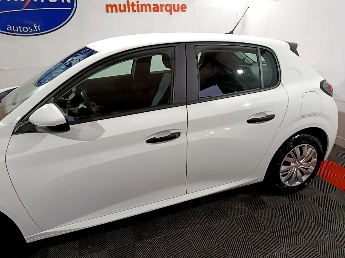 Profil côté gauche d'une Peugeot 208 blanche de 2021, avec jantes alliage et vitres teintées, en intérieur showroom.