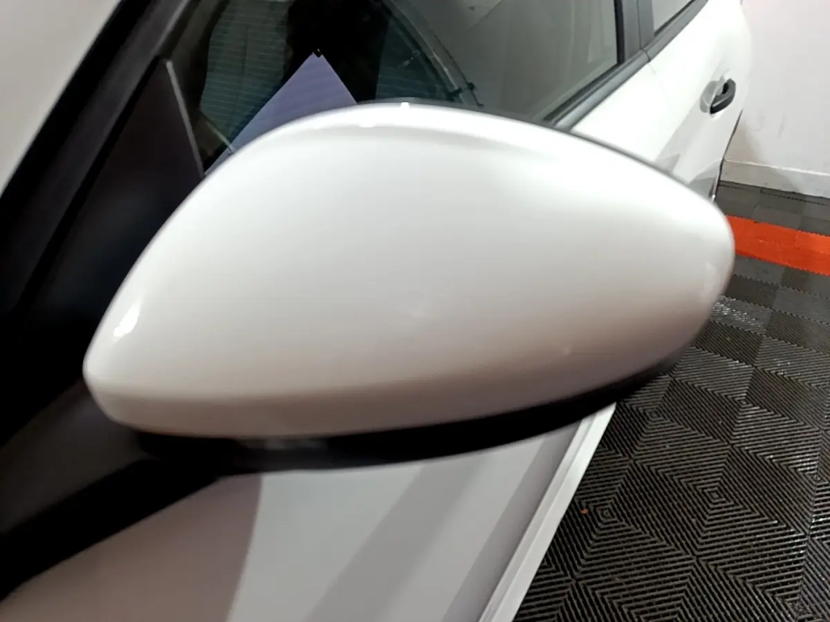 Rétroviseur côté gauche blanc d'une Peugeot 208 1.5 BlueHDi 100 S&S Premium vue en gros plan, avec portière blanche visible.