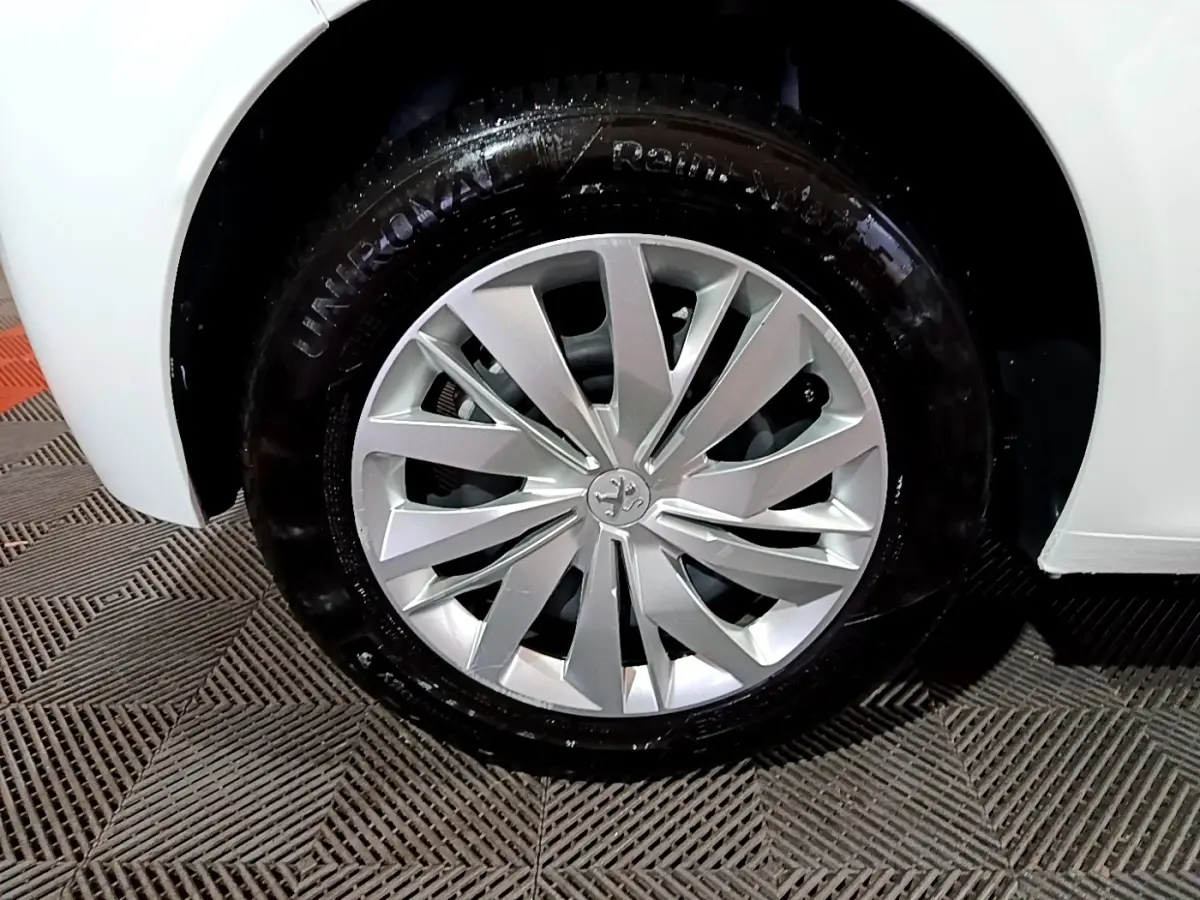 Gros plan sur la roue avant droite d’une Peugeot 208 blanche, mettant en valeur la jante alliage au design moderne.
