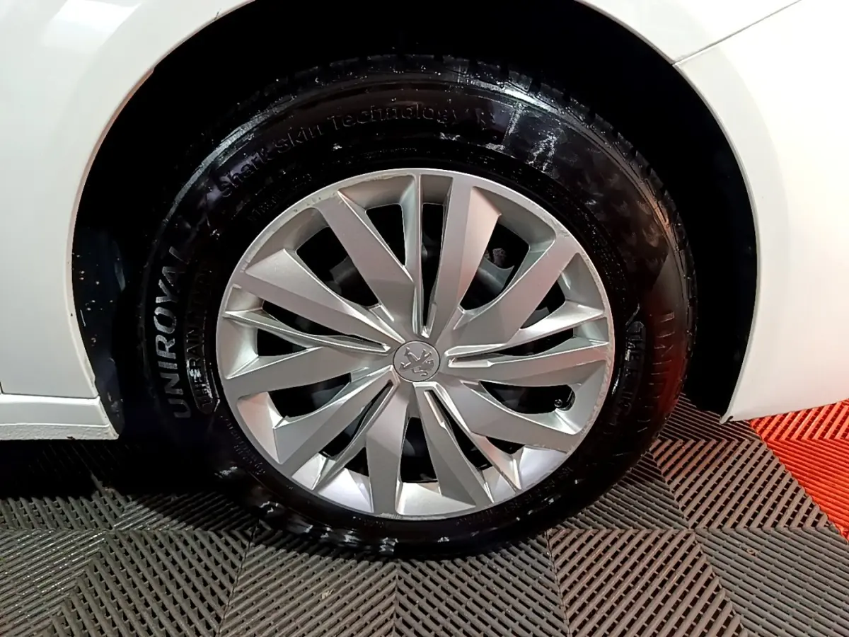 Gros plan sur la roue avant droite d'une Peugeot 208 blanche, mettant en valeur la jante alu au design moderne.