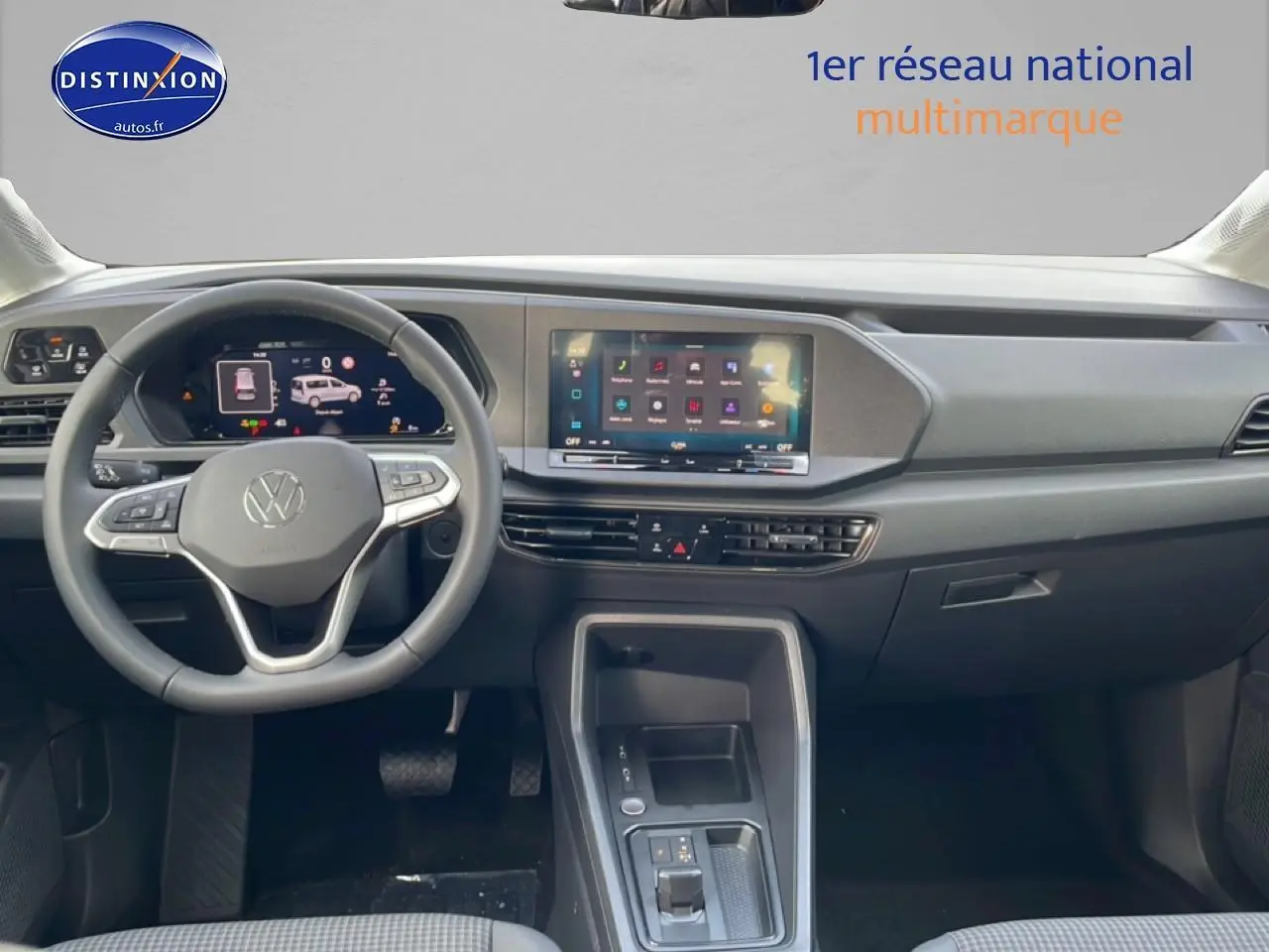 Vue intérieure frontale du tableau de bord du Volkswagen Caddy blanc 2025 avec écran tactile et volant multifonction cuir.